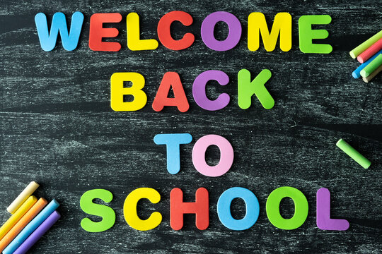Back to class. Text with coloured letters WELCOME BACK TO SCHOOL on a dark background painted in chalk. Copy space.