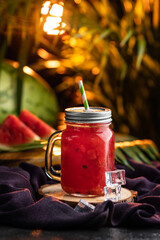 Watermelon smoothies in mason jar with ice cubes on a purple fabric, creative juice photography
