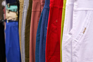 Multi-colored trousers hang on hangers in a women's clothing store.