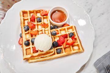Fototapeta na wymiar Classic Viennese waffles with ice cream, berries and Maple syrup. Breakfast in cafe. Table in the restaurant.