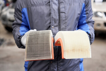 New and old dirty automotive engine air filter in the hands of an auto mechanic. Auto repair concept.