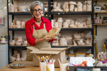 Woman seller or worker of earthenware shop packing order of client and wrapping it into paper.