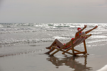 Selective focus on young Asian women wearing red bikinis and sleeping on a sunbed on a sand beach on a tropical island on a summer day holidays vacation with blue sea, beach, mountain, 