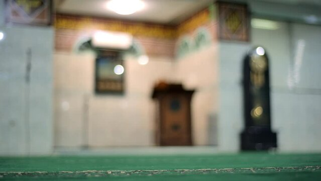 Blur image of a classic wall clock with swinging pendulum in an antique mosque of Faletehan Jakarta. Next to it is the imam's pulpit for the khutbah. Taken with a medium shot and handheld.