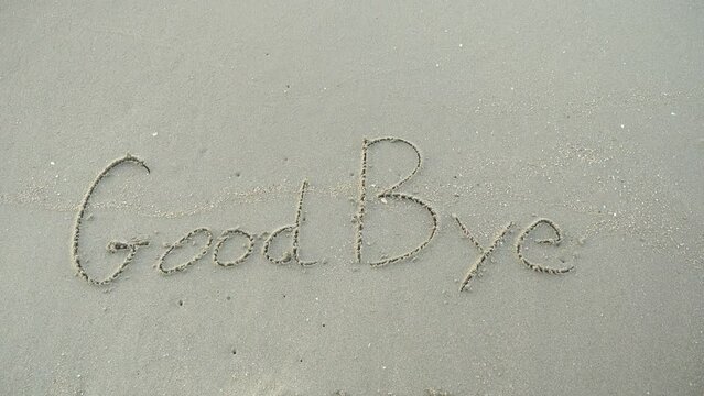Message GoodBye  written on beach sand background. 
Word Good bye lapping waves happy New Year coming concept.