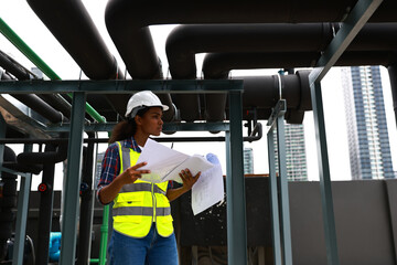 The female service engineer uses a blueprint to check and plan to monitor water treatment systems in the engineering plant