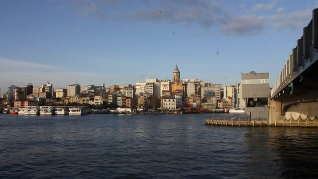 Galata tower view from the side of the Galata bridge and the shore of the Golden Horn in Istanbul, with flying seagulls