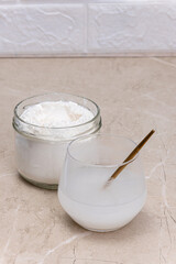 Glass of water and a jar of collagen goodnesson a marble beige background.