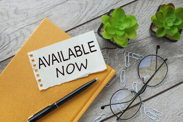 torn paper on a yellow notepad near a glass and a plant in a pot. words Available Now