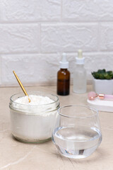 Glass of water and a jar of collagen goodnesson a marble beige background. Home beauty procedures. Drink and serums with collagen and peptides, facial care