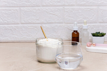 Glass of water and a jar of collagen goodnesson a marble beige background. Home beauty procedures. Drink and serums with collagen and peptides, facial care