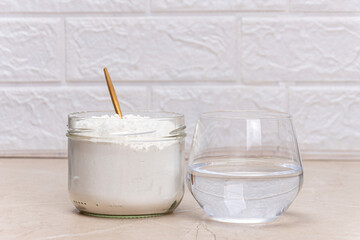 Glass of water and a jar of collagen goodnesson a marble beige background.