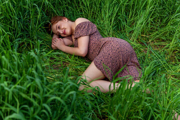 A young girl in a beautiful dress lies in the green grass