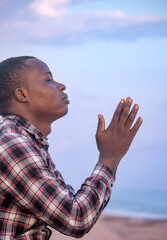 An evocative image capturing the peace and devotion of a Christian individual, their hands raised in prayer, their profile outlined against the tranquil blue hues of the sky, 