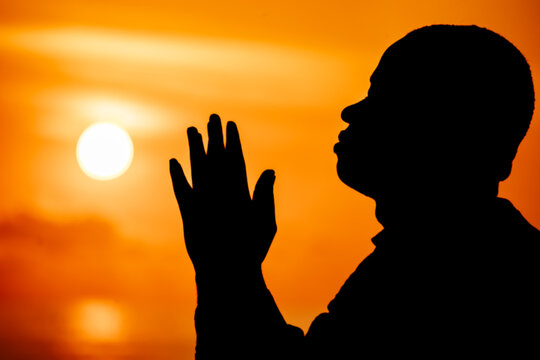 An inspiring image of a Christian worshipper, his silhouette illuminated against the beautiful solstice sky, his outstretched hands a visual representation of his deep connection with Jesus.