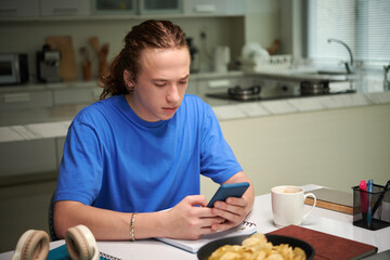 Student drinking morning coffee and checking social media on smartphone