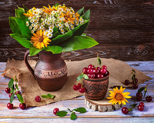 Ripe cherries in a vintage cup. Summer still life with a bouquet of wildflowers in a vintage vase on a wooden background