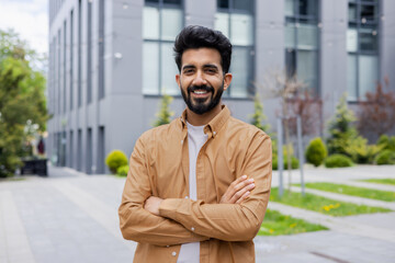 Portrait of young Hindu programmer, man outside office building with crossed arms smiling and looking at camera, businessman in shirt.