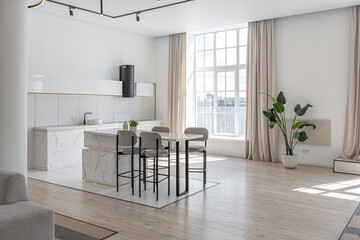 kitchen and dining island with high bar stools in a minimalistic modern luxury design of an expensive house on a sunny day. white walls with plaster, parquet, decorative lighting and no one inside