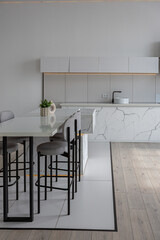 kitchen and dining island with high bar stools in a minimalistic modern luxury design of an expensive house on a sunny day. white walls with plaster, parquet, decorative lighting and no one inside