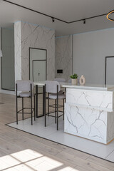 kitchen and dining island with high bar stools in a minimalistic modern luxury design of an expensive house on a sunny day. white walls with plaster, parquet, decorative lighting and no one inside