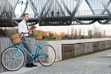 Business man with vintage bicycle by the river reading a book