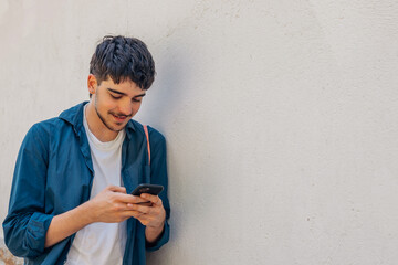 young man with mobile phone and backpack isolated on wall in the street outdoors