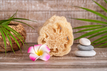Natural vegetable Loofah sponge for bath and shower is decorated with Zen stones and a palm branch. Skin and body care. Beige wooden background.