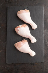 Raw chicken legs on a black slate cutting board on a black concrete background. Top view, close up.