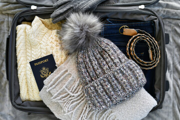Suitcase flat lay packing for cold weather travel trip sweater, warm scarf, knit stocking cap hat