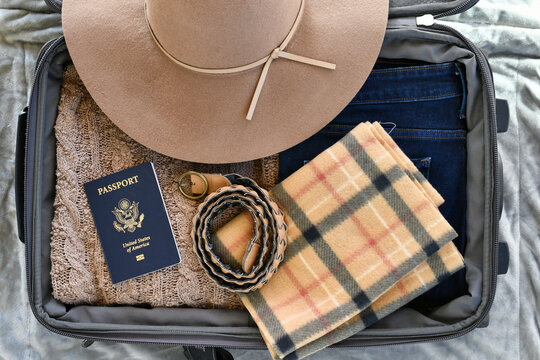 Suitcase flat lay packing for cold weather travel trip sweater, warm scarf, wide brim hat passport