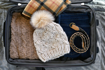 Suitcase flat lay packing for cold weather travel trip sweater, warm scarf, knit stocking cap hat