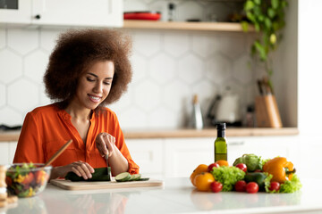 Portrait of happy black woman cooking healthy lunch in kitchen interior