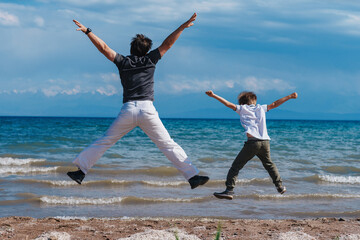 Happy father and son jumping on shore of the lake