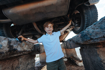 Cute boy automotive mechanic standing under car bottom with wrench