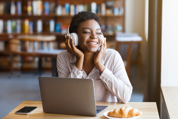 Black woman listening to music with headset, laptop in cafe