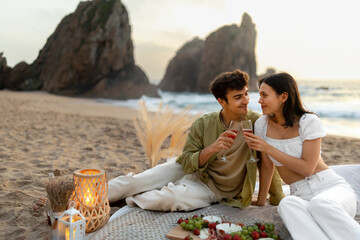 Coastal clinks. Young romantic couple having picnic on sandy beach, drinking wine and enjoying date at coastline
