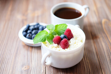 Cottage cheese and berryies in a bowl on a table with a cup of coffee.