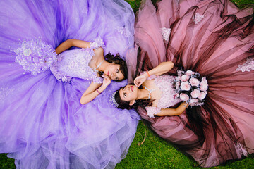 Portrait of Mexican quinceanera teenagers lying on the grass looking into each other's eyes