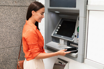 Fototapeta na wymiar Lady using smartphone gaining access to ATM withdrawing money outside