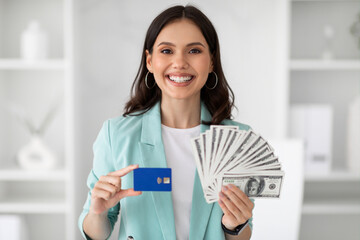 Glad young european woman in suit shows credit card and lot of money, enjoy victory