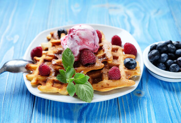 Waffles with ice cream and raspberries for breakfast over blue wooden table.