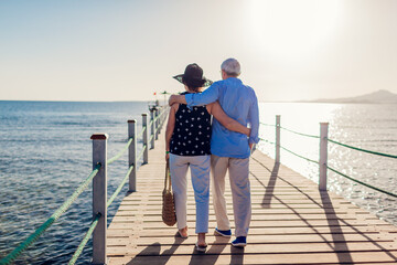 Senior family couple walking on seacoast pier. Elderly people enjoying summer vacation on seaside.