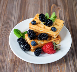 Waffles with blackberries for breakfast on white plate over wooden table.