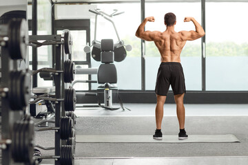 Rear view of a shirtless musuclar man flexing back muscles at the gym