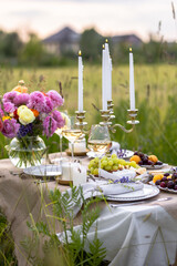 Summer sunset, romantic date outdoors in meadow, marriage proposal. Romantic sunset dinner in the field. Table honeymoon set for two with luxurious food, glasses of champagne drinks in a restaurant.