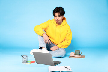 Asian student guy sitting with laptop learning on blue background