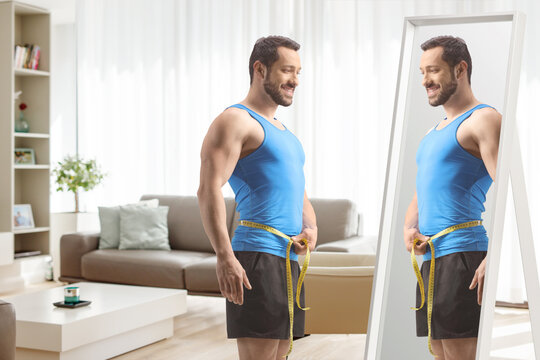 Man in sportswear measuring waist in front of a mirror at home