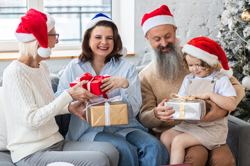 Fototapeta premium Happy smiling family near beautiful Christmas new year tree exchanging gifts in the morning. Grandmother, grandfather, daughter and granddaughter celebrating holidays at home together