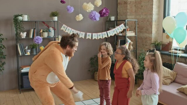 Medium shot of young Caucasian party entertainer in cat costume giving preteen girl birthday present, asking to shake box to guess what is inside, and happy kids laughing and smiling